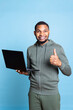 © DC Studio - African american young guy typing on his laptop against blue background, composing emails and working on paperwork. Male overjoyed person multitasking in studio, cheerful adult.