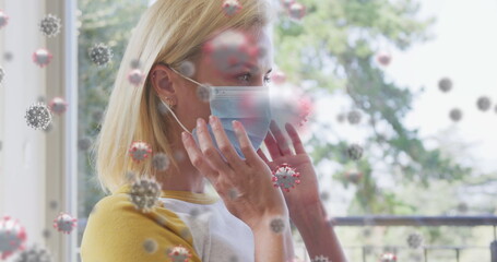 Poster - Image of covid 19 cells over caucasian blonde woman putting face mask on