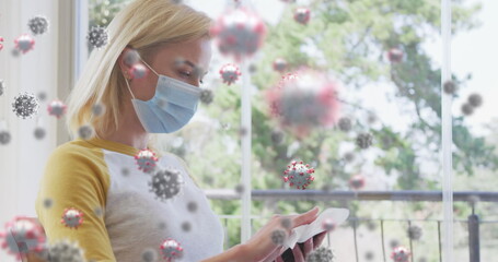 Poster - Image of covid 19 cells over caucasian blonde woman wearing face mask using smartphone