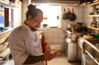© Marko Geber - Sushi chef using smartphone in restaurant kitchen