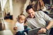 © Geber86 - Father and son using a digital tablet at home while the mother is behind them on the couch