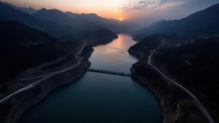 Poster - Panoramic view of river flowing through mountainous landscape at sunset. The river is surrounded by green hills and trees, with a golden sun setting in the distance, casting a warm glow over the