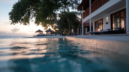 Poster - A tranquil view of turquoise water from an infinity pool, leading to a sandy beach with palm trees under a soft sunset. A villa with warm light adds to the peaceful coastal scene, evoking a sense of