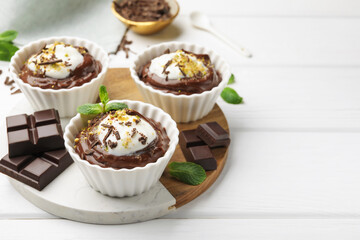 Wall Mural - tasty pudding with whipped cream in bowls and pieces of chocolate on white wooden table, space for t
