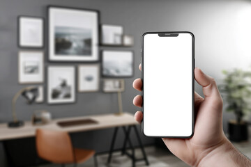 Aufkleber - Hand holding smartphone with blank screen, against blurred background of home office with framed pictures and desk Mockup for app presentation