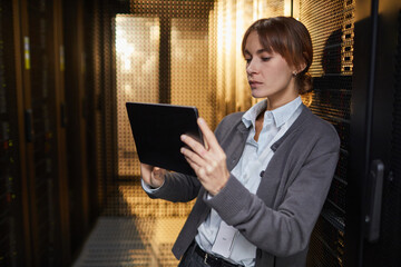 Poster - Caucasian IT professional examining data on tablet while standing in server room setting, surrounded by server racks and tech equipment