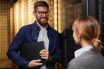 Poster - Smiling IT professional holding laptop while talking with colleague in server room surrounded by network equipment working on project