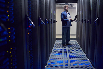 Poster - Male technician standing in data center while using laptop for server performance monitoring and maintenance