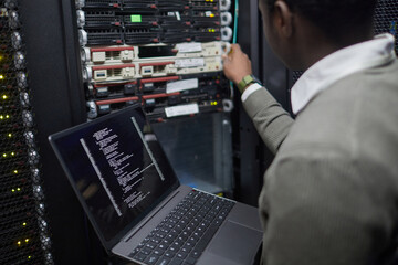 Poster - Person managing server equipment in a technology environment, checking system status on a laptop. Focus on information technology and network administration