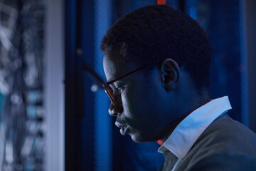 Poster - Profile view of a dedicated technician examining computer network in a server room under low light. Intense concentration on technological equipment