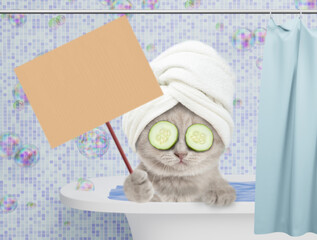 Leinwandbilder - Cute kitten with towel on it head and slices of cucumber on it eyes takes the bath at home and shows blank placard on wooden stick. Empty space for text