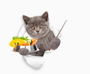 Poster - Funny kitten holds the bowl of vegetables, looks through the hole in white paper and points away on empty space