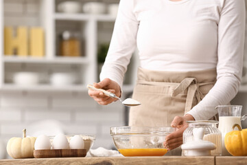 Wall Mural - woman adding spoon of sugar into bowl with eggs at table in kitchen. closeup