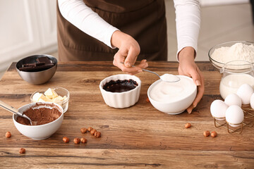 Wall Mural - woman preparing chocolate brownie with spoon of sugar at table in kitchen. closeup