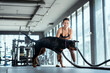 © 2B - Woman exercises with dog using battle ropes in a modern gym environment during daytime