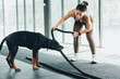 © 2B - Woman exercises with dog using battle ropes in a modern gym environment during daytime