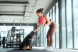 © 2B - Woman exercises with a weighted ball while a dog watches in a modern gym setting during a daytime workout