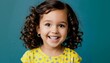 © KarpenArt Studio - a cheerful young girl with curly brown hair and a bright smile poses for a portrait against a solid blue background.