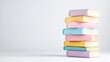 © danadesa - Neat stack of pastel colored books stands on a clean white surface in a bright minimalist studio setting.