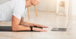 © Prostock-studio - Personal coach online. Serious guy makes plank on mat and looks at laptop in interior of home, profile, free space