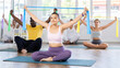 © JackF - Asian girl conduct Pilates class for multinational group, sitting with wide elastic band in hands above head makes body bends. She leans left right from sitting position with resistance band in hands