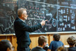 © Starmarpro - A professor explains a concept to students in a lecture hall. He's standing in front of a chalkboard covered in complex formulas and diagrams. The students listen attentively in academic setting.