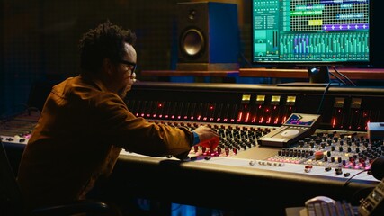 Leinwandbilder - African american audio expert adding sound effects on tracks in post production, operating mixing console and pushing sliders. Producer creating music for his new album, audio mixer. Camera A.