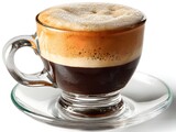 A delicious cup of macchiato coffee sits on a clear glass saucer ready to be enjoyed.