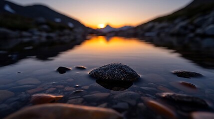 Poster - A low angle captures a reflective lake mirroring a vibrant sunset with a prominent rock formation at center surrounded by mountains in soft focus