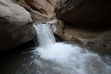 Aufkleber - Waterfall cascading into a natural pool within a canyon. The image captures the movement of water with a focus on texture and geological formations
