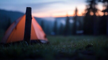 Aufkleber - Orange tent near wooden post on green grass with blurred forest and sunset background at twilight