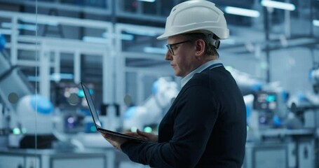 Fototapete - Computer Monitors Display Robotic Operations and Data Analytics. Engineer in a Hard Hat Working in an Industrial Facility, Using Laptop Computer to Monitor Robotic Arms in a Futuristic Factory