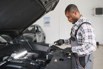 Poster - Portrait of smiling mechanic in car service ordering new parts for damaged vehicle using tablet. African american repairman looking online for components to replace old ones in busted automobile