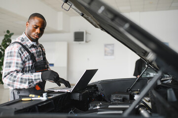 Poster - Black auto mechanic running diagnostic on laptop while analyzing engine problems in a workshop