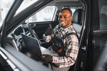 Poster - Portrait of smiling mechanic in car service ordering new parts for damaged vehicle using tablet. African american repairman looking online for components to replace old ones in busted automobile