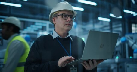 Fototapete - Middle Aged Male Engineer in a Hard Hat Using a Laptop Computer to Monitor Robotic Arms in an Advanced Industrial Factory. Industrial Manager Overlooking Modern Automated Electronics Manufacturing