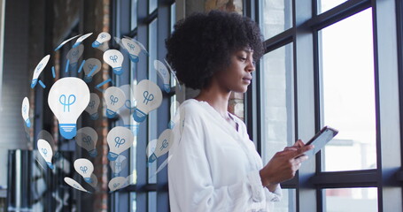 Poster - Image of globe of light bulb icons over african american woman using tablet