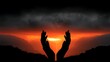 © Big9869 - Two Hands Reaching for the Dramatic Fiery Sunset Silhouette Against a Mountainous Landscape.