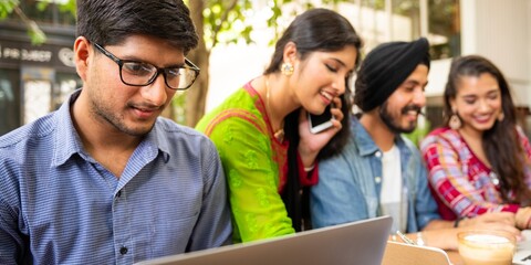 Poster - Group of young adults working together outdoors. Diverse team collaborating. Casual setting with laptops and phones. Teamwork and collaboration in action. Indian students working together outdoors.
