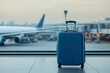 © Harmony Studio - A blue suitcase stands alone in an airport terminal by the window, with planes visible outside