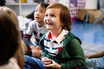 Poster - Happy Caucasian boy smiling and sitting with other children in classroom. Boy in classroom with other children. Student boy enjoy lesson in classroom. Student boy smiling in classroom with other kids