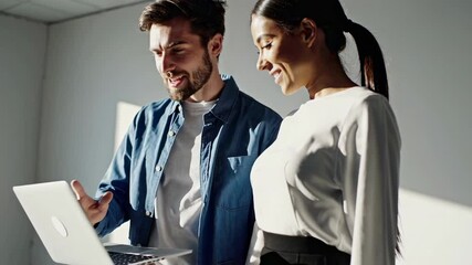 Aufkleber - Two business colleagues, a man and a woman, are standing and working together on a laptop, discussing a project in a naturally lit office space