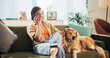 © peopleimages.com - Happy, phone call and woman with dog on sofa for bonding, care and relax together in living room. Chill, pet and person with Golden Retriever on smartphone for chat, social networking and contact