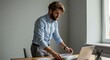 © Strive Studio - Man stands at desk reviewing documents next to laptop in office setting.