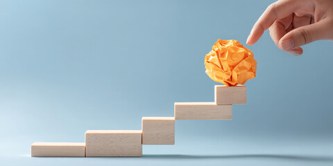Poster - Yellow crumpled paper ball atop wooden blocks staircase, hand reaching, light blue background, showcasing growth, achievement, and progress concept