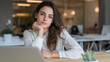 © Inspire Shots Hub - Young woman with brown hair, wearing white shirt, sits at wooden desk, looking at camera. Image showcases confidence and professionalism in modern office setting