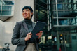 © Zamrznuti tonovi - Smiling businesswoman holding tablet and looking away outside office building