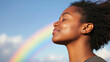 © Yanwei - happy young black woman breathing fresh air outdoors in nature. african american female meditating outside practicing wellness meditating deep breathing. blue sky and rainbow. inclusive pride