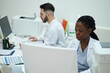 © DragonImages - Medical professionals working in a lab environment, analyzing data on computer screens while discussing procedures. Laboratory equipment and documents visible in background