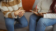© Krakenimages.com - Two women friends talking indoors in a cozy living room setting, one writing in a notebook, showcasing a casual and warm environment for conversation and connection.